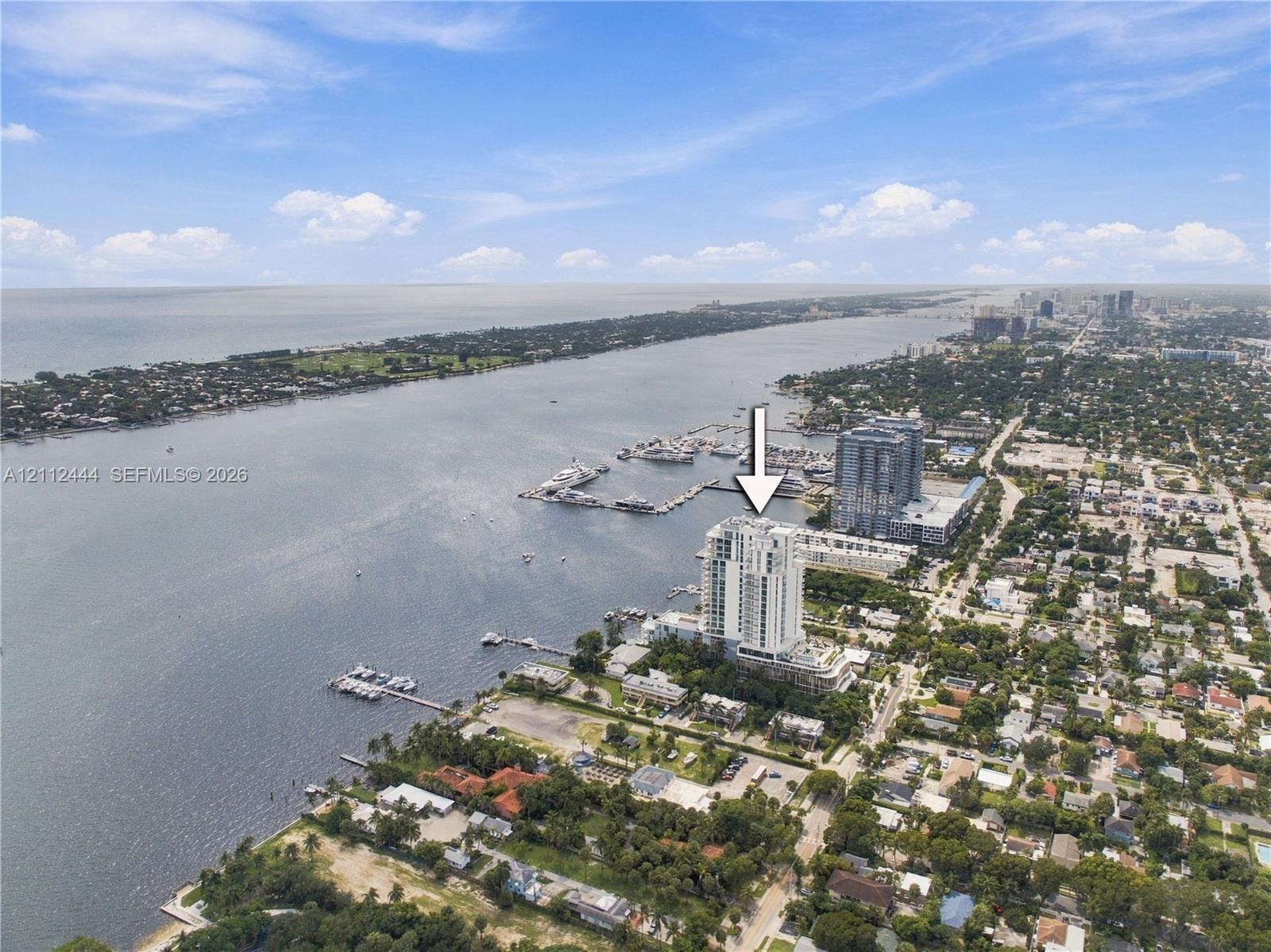 Aerial perspective of a high-rise tower situated on a coastal waterfront featuring direct proximity to a marina and expansive water scenery