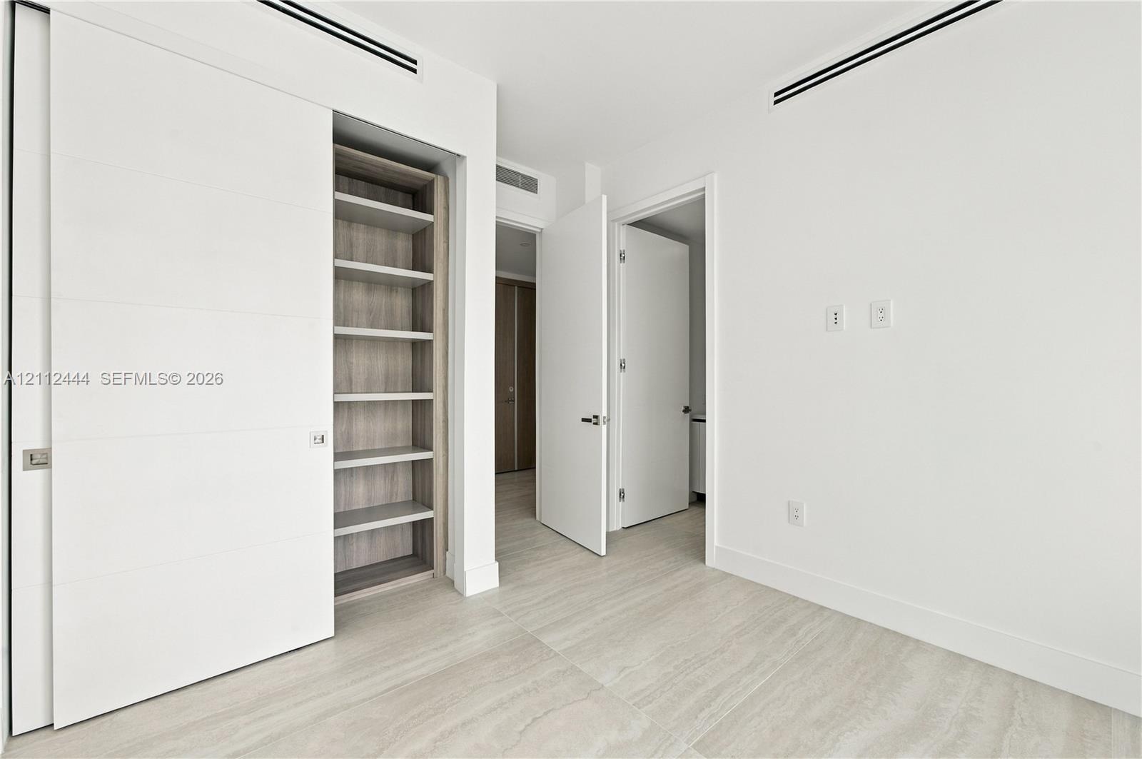 Minimalist interior featuring wood-finish flooring, recessed linear ceiling diffusers, sliding panel doors, and built-in shelving with wood-tone inter