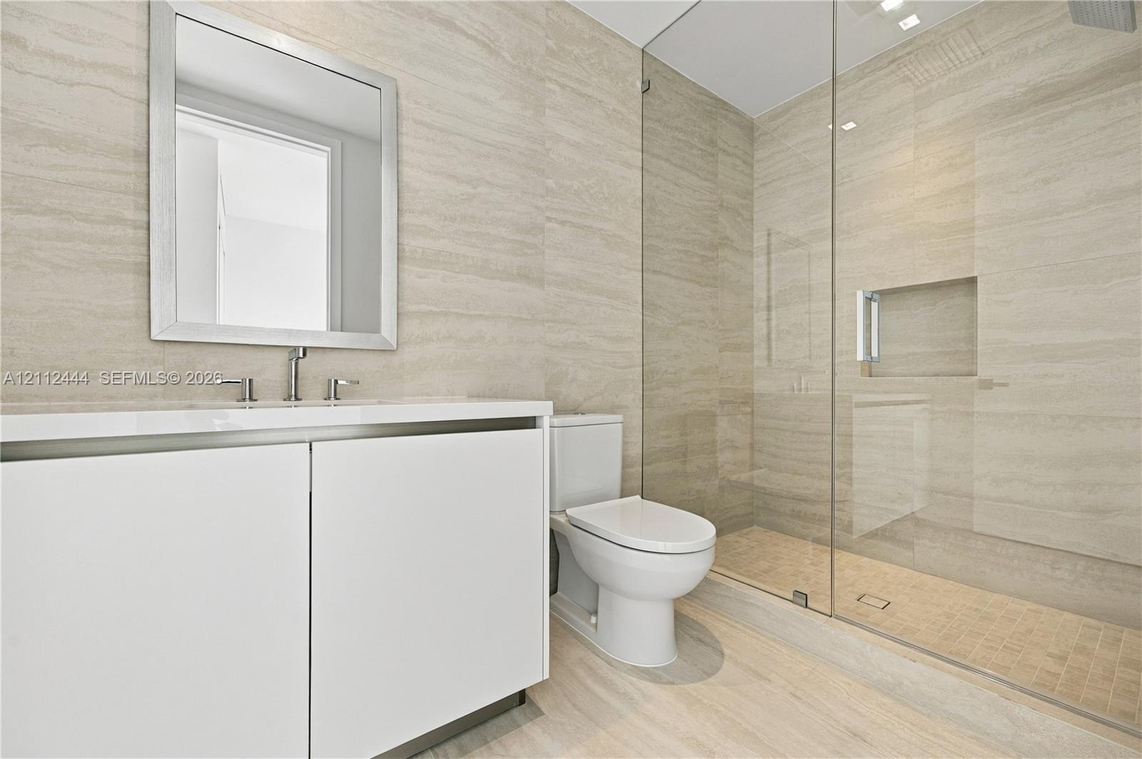 Minimalist vanity featuring a smooth-finish white cabinet and rectangular sink with metal fixtures, complemented by wall-to-wall linear-patterned tile