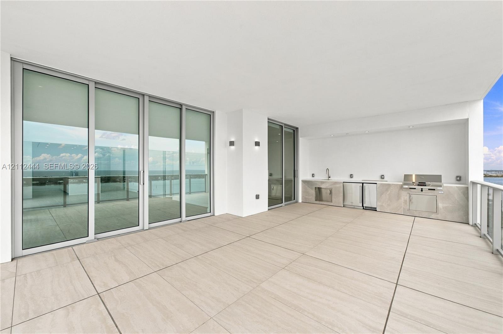Expansive covered terrace featuring large-format tile flooring, a built-in outdoor kitchen with stainless steel appliances, stone-finish cabinetry, fl