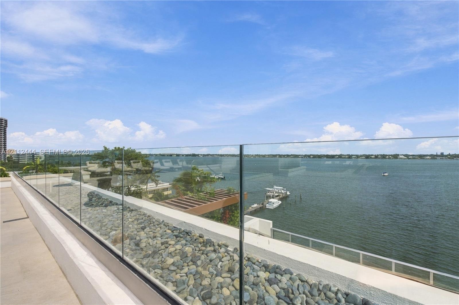 Elevated balcony featuring a frameless glass railing, stone-finished flooring, and water frontage