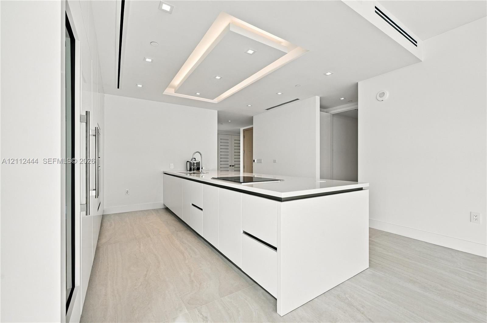 Minimalist kitchen featuring matte white flat-panel cabinetry, a quartz waterfall-edge island, an integrated induction cooktop, recessed lighting, and