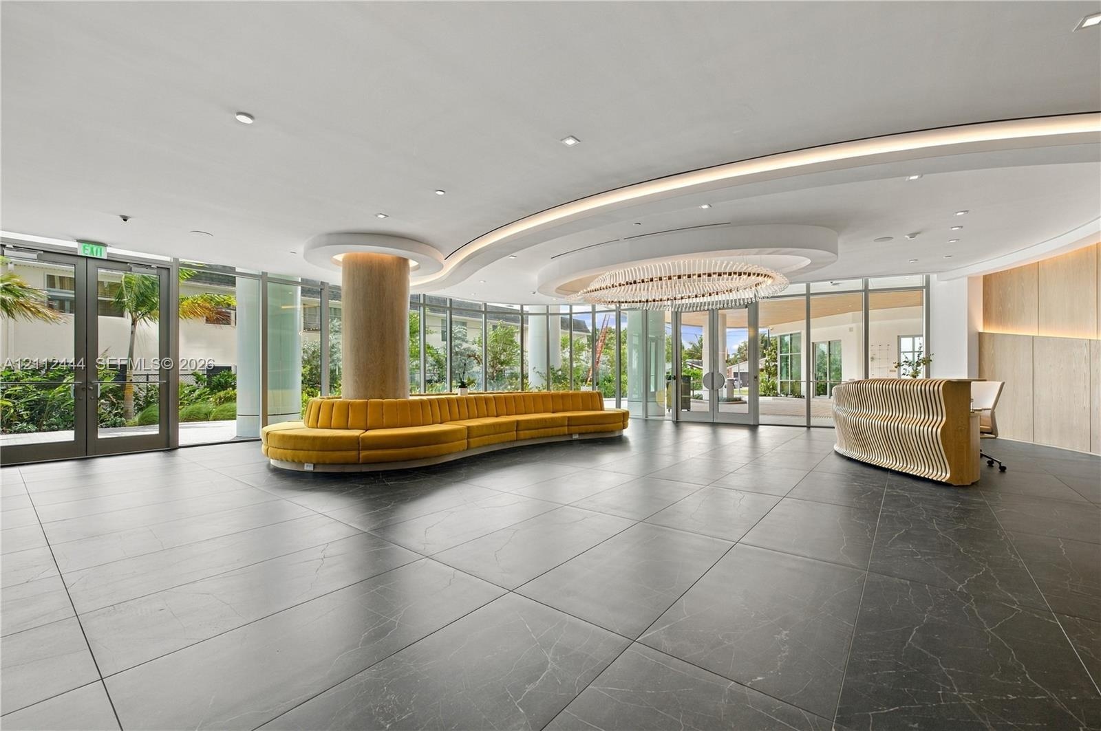 Lobby featuring large-format dark stone flooring, floor-to-ceiling glass walls, recessed cove lighting, and a circular chandelier