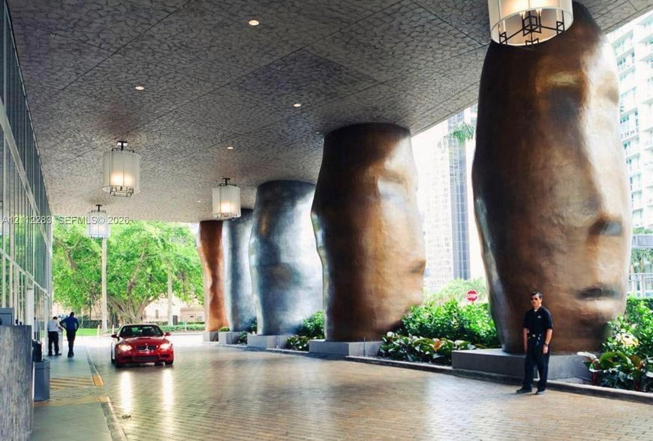 Covered porte-cochere featuring monumental sculptural columns, paved driveway, recessed ceiling lighting, and hanging pendant fixtures