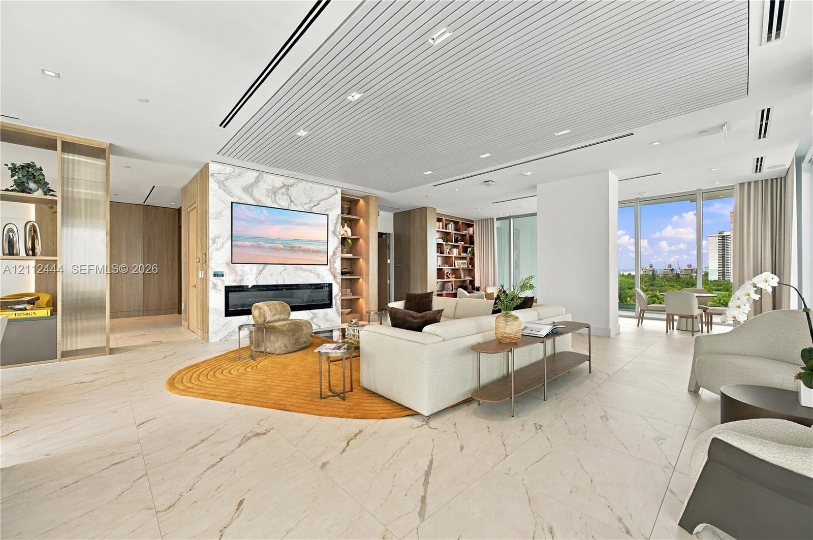 Open-concept interior featuring large-format tile flooring, a floor-to-ceiling stone-clad fireplace wall, custom built-in shelving, a tiered slatted c