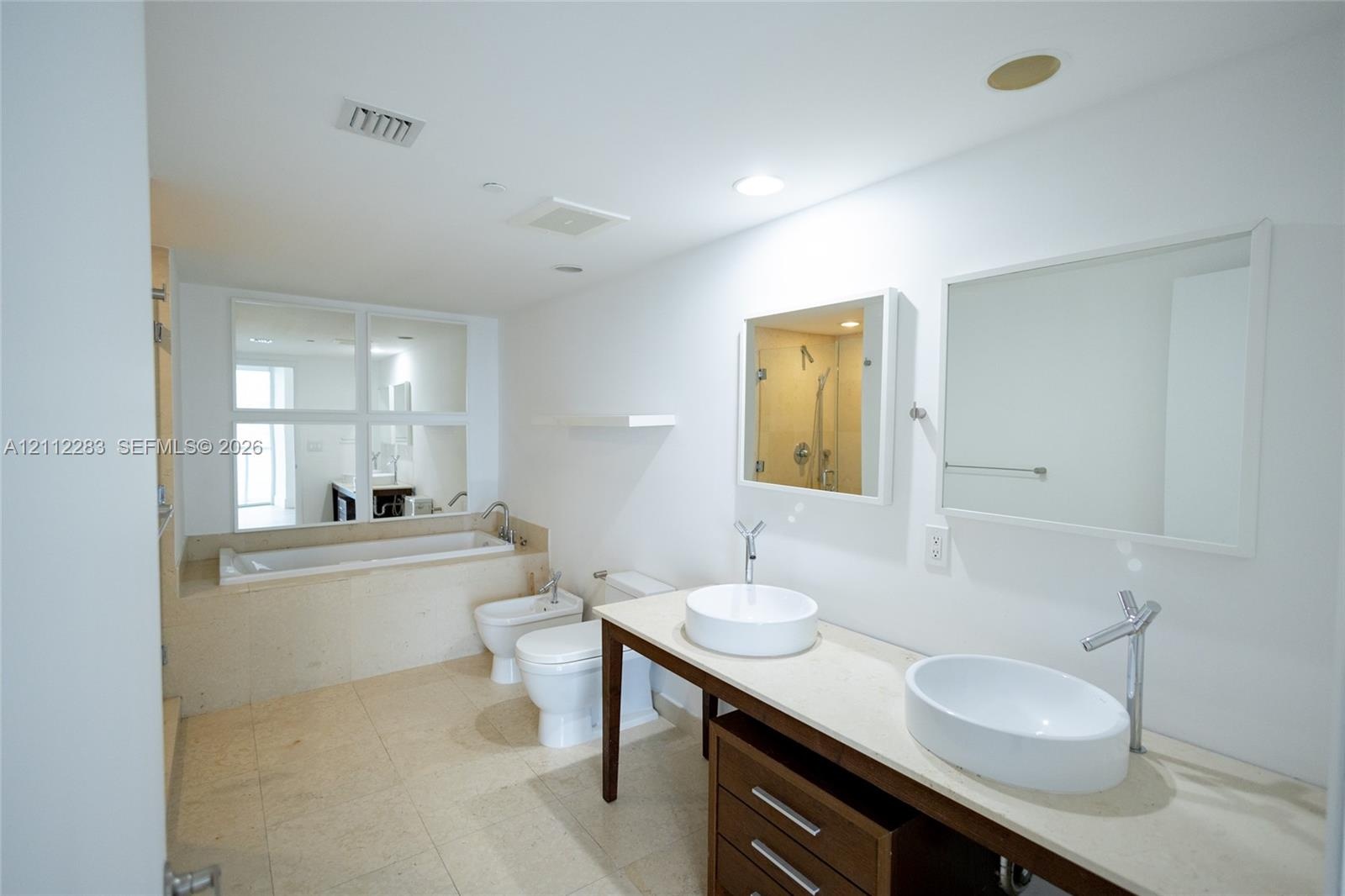 Double vanity featuring two oval vessel sinks, stone-finish countertop, dark wood cabinetry, and wall-mounted mirrors, complemented by a drop-in soaki