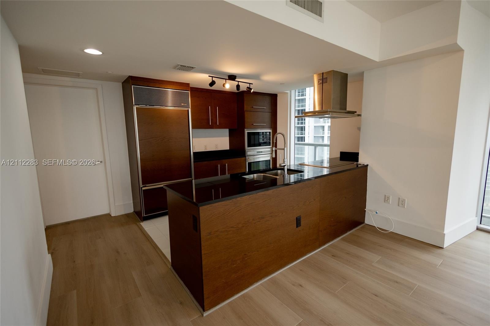Kitchen featuring wood-finish cabinetry, dark stone countertops, stainless steel appliances including a built-in refrigerator and wall oven, and a cen