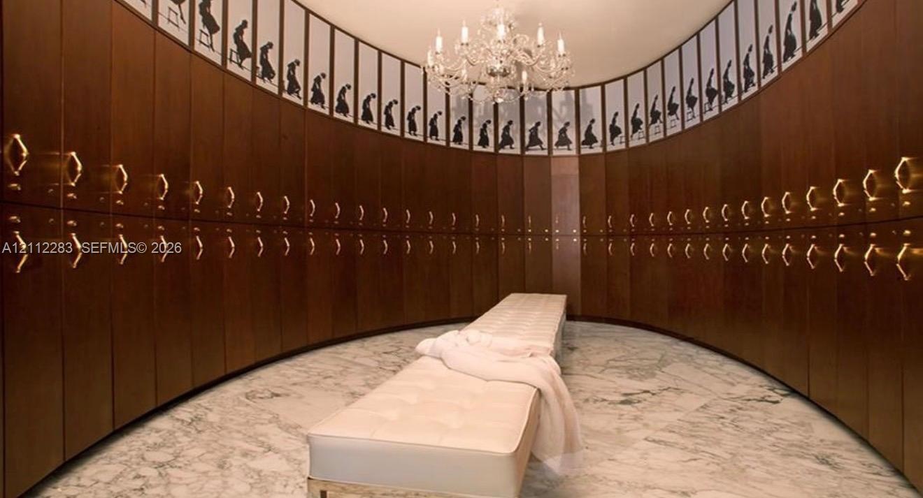 Curved wood cabinetry featuring brass hardware, polished stone flooring, and a multi-tiered crystal chandelier