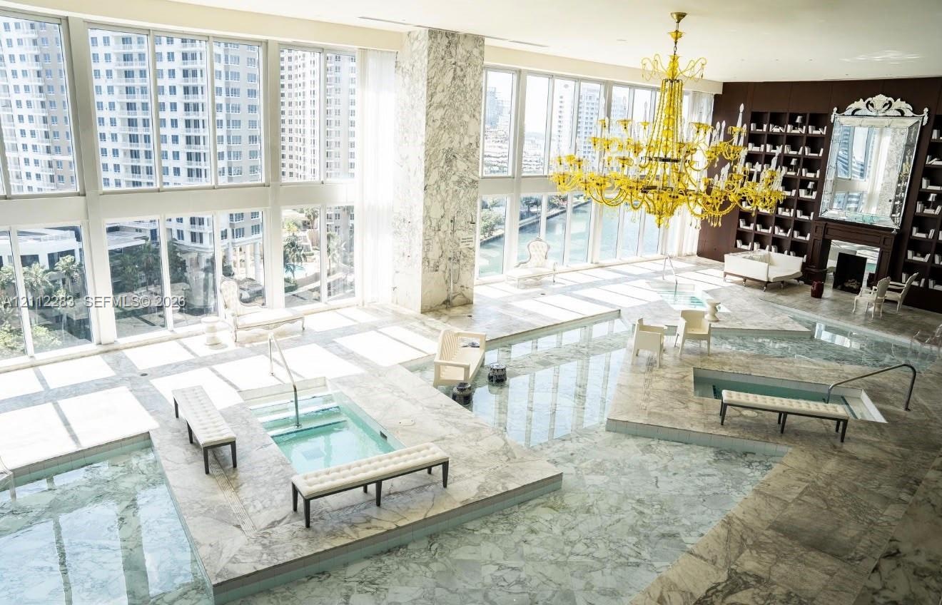 Floor-to-ceiling windows, stone-clad flooring, multiple sunken spa basins, an expansive tiered stone deck, and a feature wall with integrated floor-to