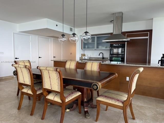 Kitchen featuring stone countertops, integrated wood-toned cabinetry, stainless steel range hood, glass-front upper cabinets, and glass globe pendant 