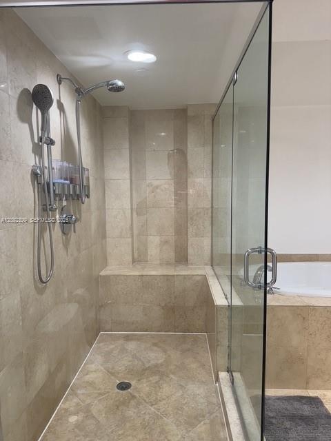 Walk-in shower featuring floor-to-ceiling neutral tile, built-in tiled bench, frameless glass enclosure, and dual-head rainfall and handheld shower fi
