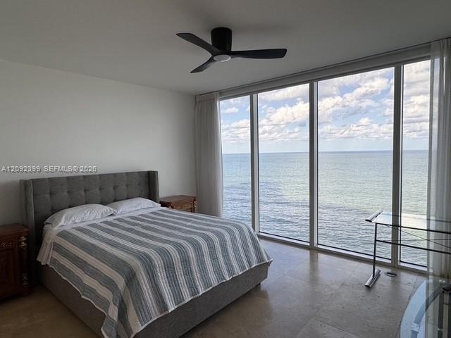 Floor-to-ceiling windows featuring ocean scenery, matte black ceiling fan, and stone flooring