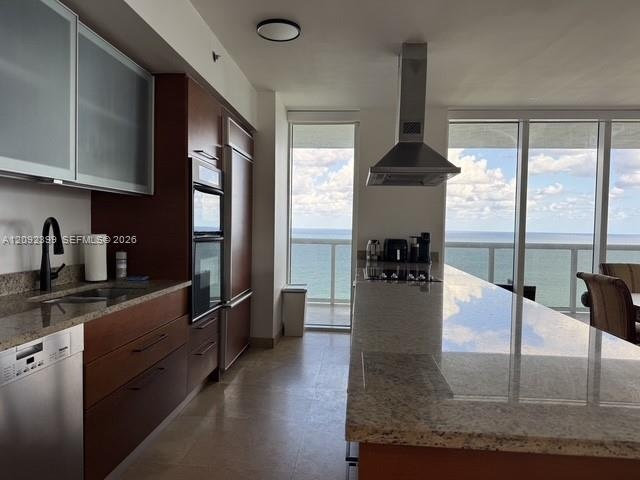 Kitchen featuring floor-to-ceiling windows with ocean scenery, an expansive stone-surface island, wood-finish cabinetry with frosted glass upper doors