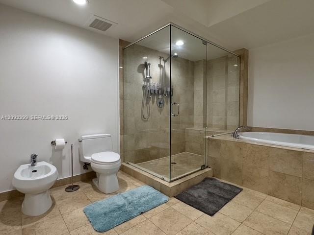Frameless glass shower enclosure with stone wall tile, separate soaking tub with stone surround, bidet, and neutral floor tile