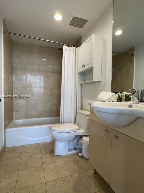 Bathroom featuring a tub-shower combination with tile surround, a wall-mounted storage cabinet, a vanity with a drop-in sink, and stone-finish floorin
