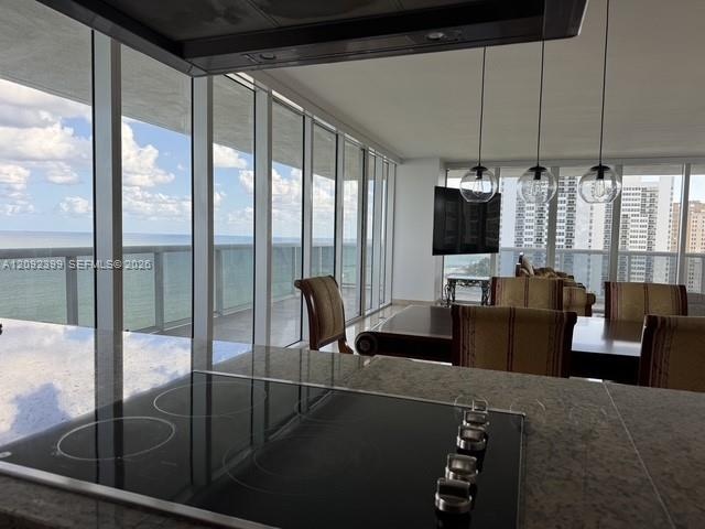 Floor-to-ceiling windows, natural stone countertop with integrated electric cooktop, three glass globe pendant lights, and an expansive balcony with m