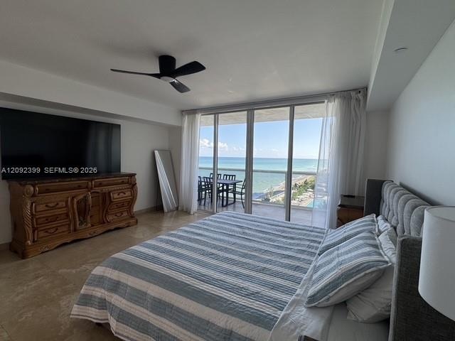 Floor-to-ceiling glass sliders, stone tile flooring, ceiling fan, and private balcony overlooking the ocean