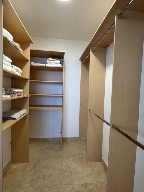 Walk-in closet featuring light wood-finish shelving, multiple open storage tiers, integrated metal clothing rods, and tile flooring