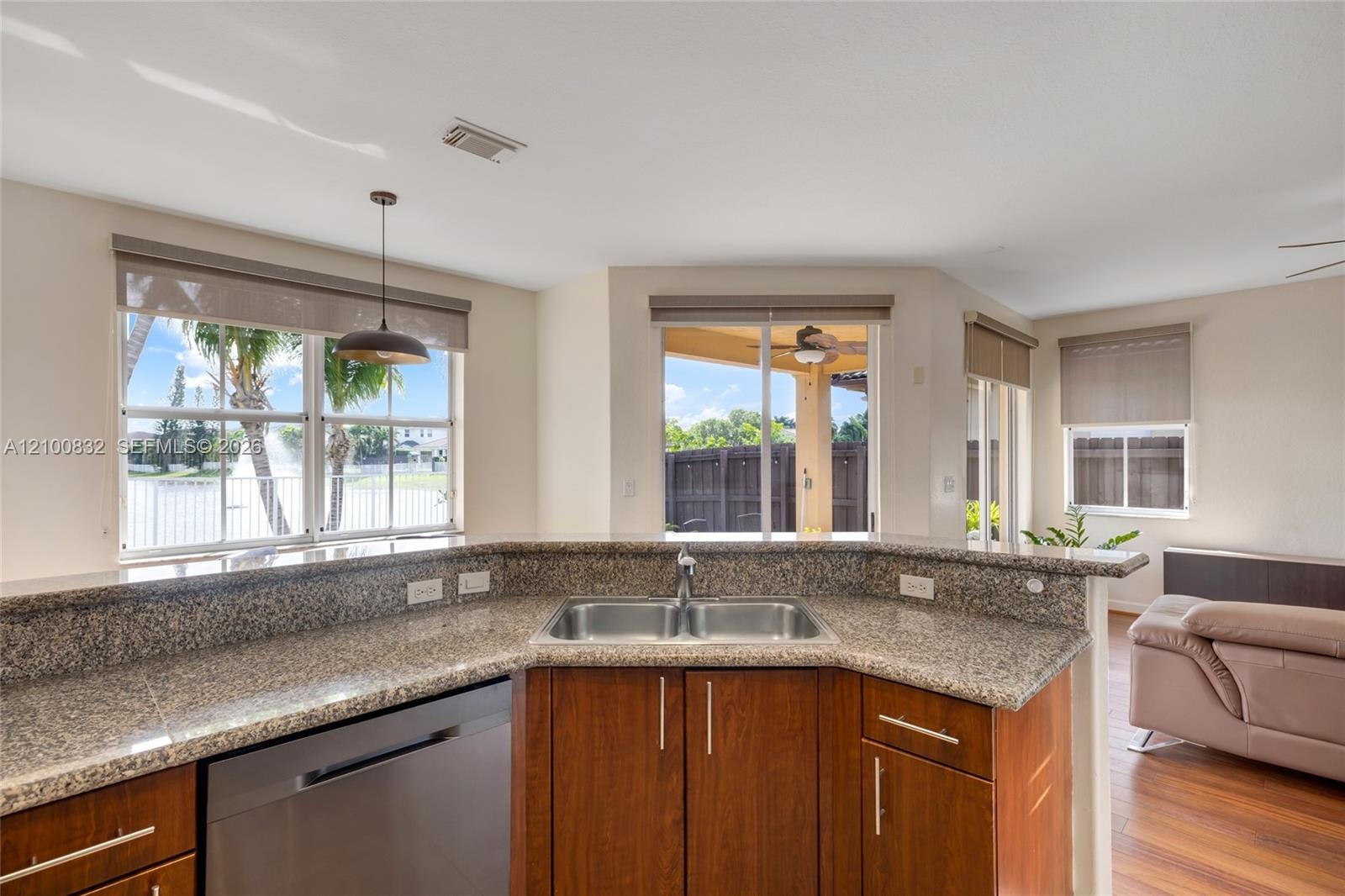 Kitchen featuring stone-finish countertops, stainless steel dual-basin sink, wood-finish cabinetry, built-in dishwasher, and multiple windows
