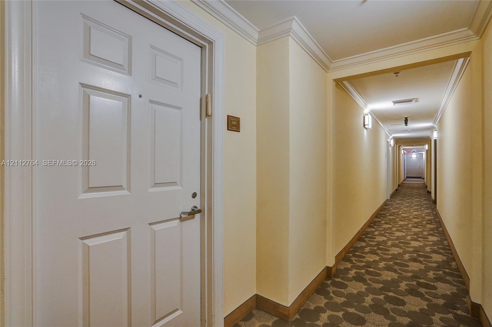 Interior corridor featuring six-panel door with metal hardware, crown molding, and patterned carpeting