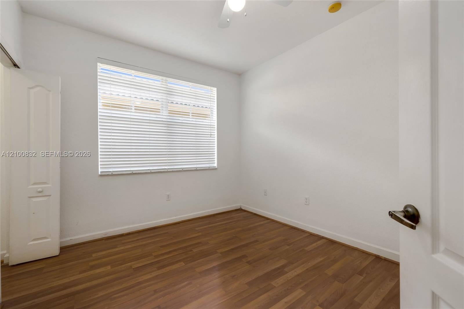 Interior space featuring wood-finish flooring, a window with horizontal blinds, a ceiling fan, and a built-in closet with a paneled door
