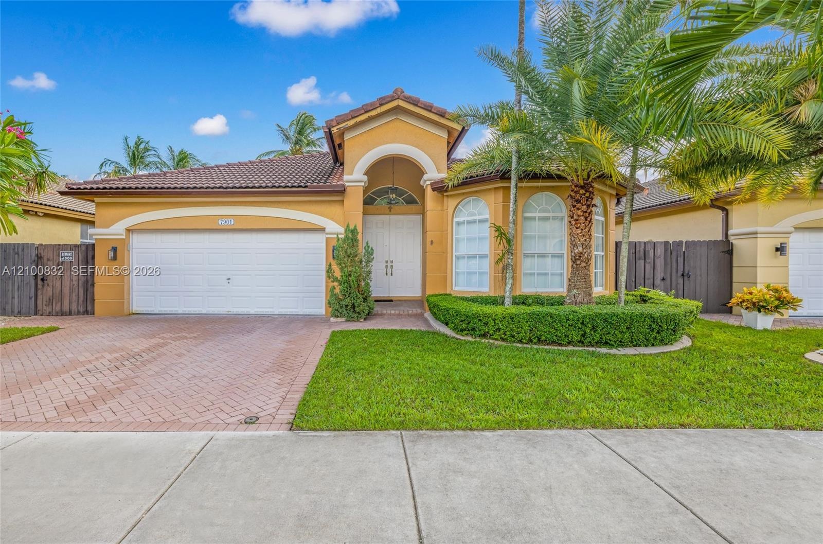 Stucco exterior featuring a tiled roof, arched entryway, paved driveway, and manicured landscaping