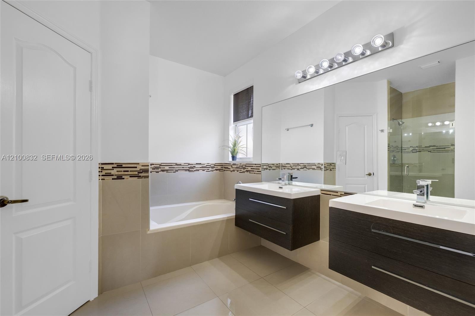 Dual floating vanity with rectangular sinks and chrome faucets, large frameless wall mirror, six-light vanity fixture, built-in soaking tub, and tile 