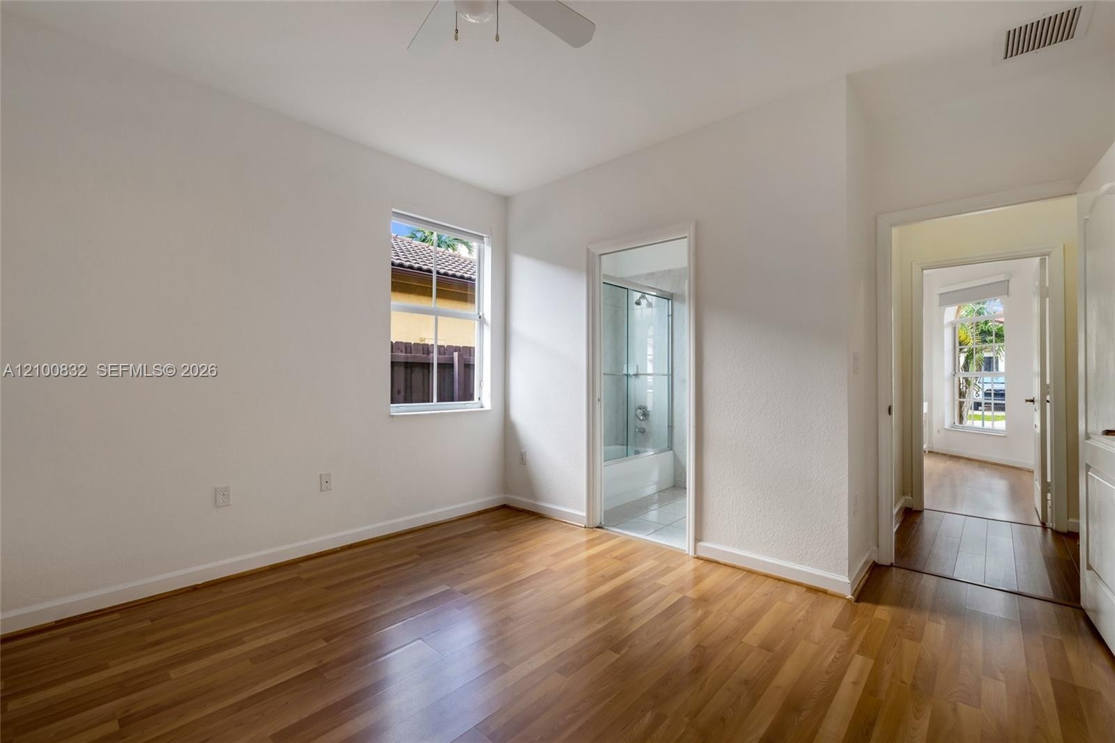 Room featuring wood-finish flooring, a ceiling fan, a window, and an attached bathroom with a shower-tub combination