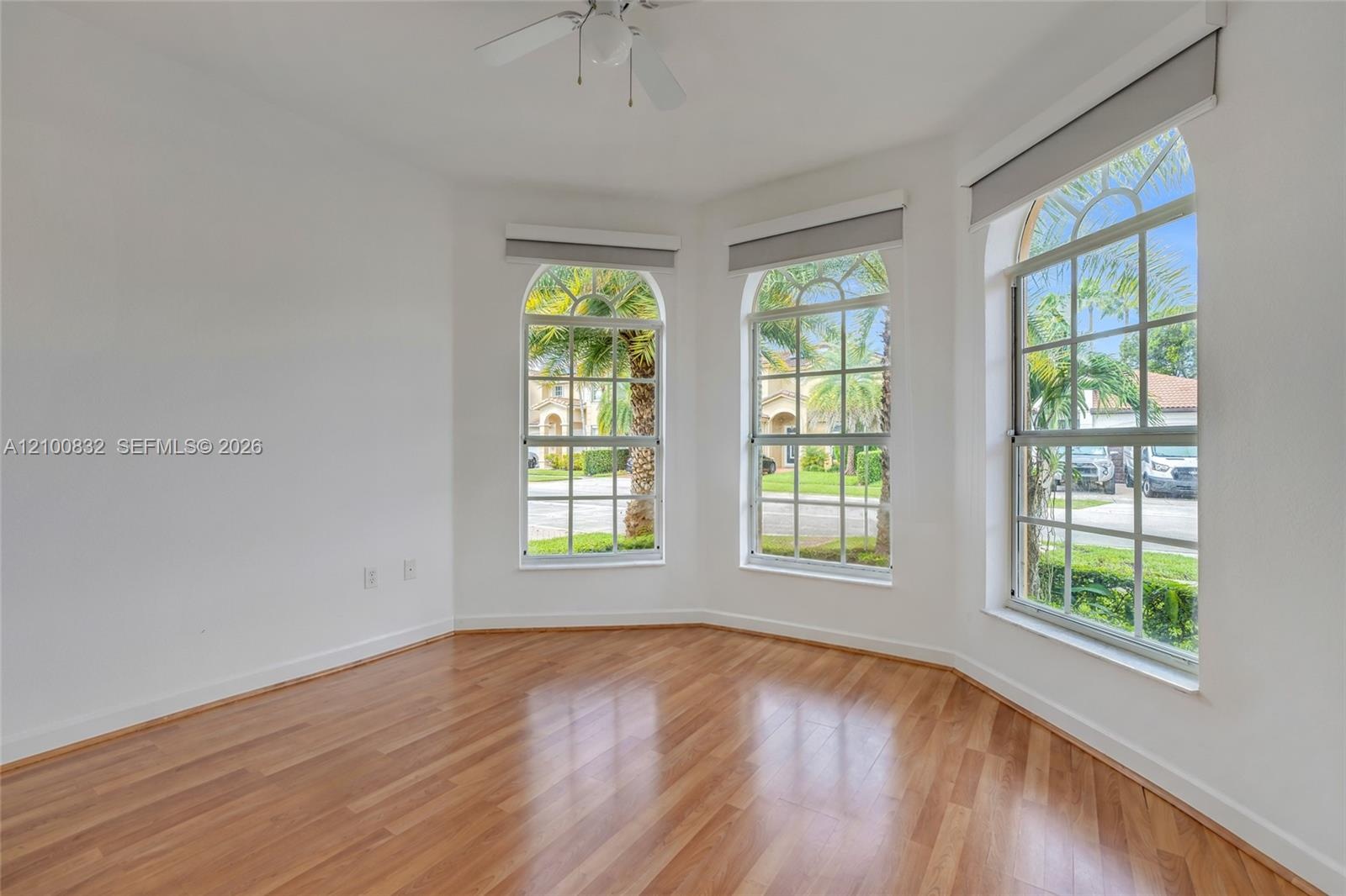 Bay window featuring three arched panes, wood-finish flooring, and a ceiling-mounted fan