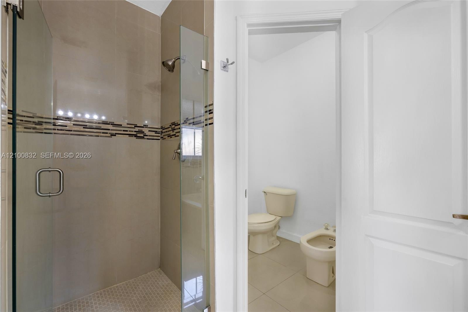 Walk-in shower with a glass enclosure, floor-to-ceiling tile, and a decorative tile inlay, featuring a separate water closet with a porcelain toilet a