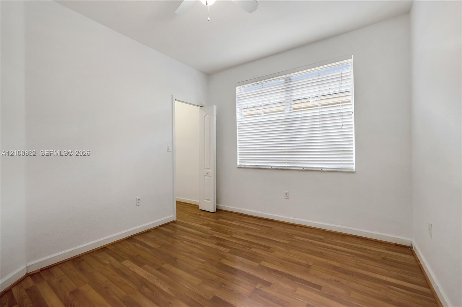 Interior room featuring wood-finish flooring, a ceiling fan, and a window with horizontal blinds