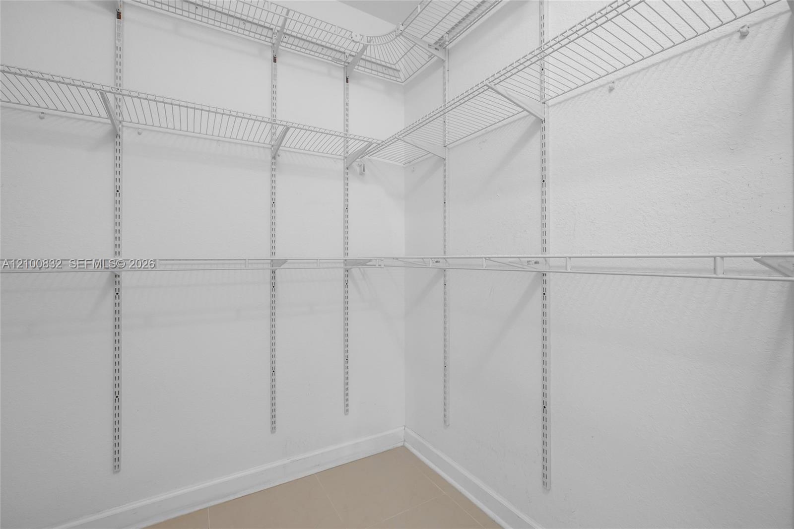 Walk-in closet featuring white wire shelving, multi-level storage racks, and neutral tile flooring