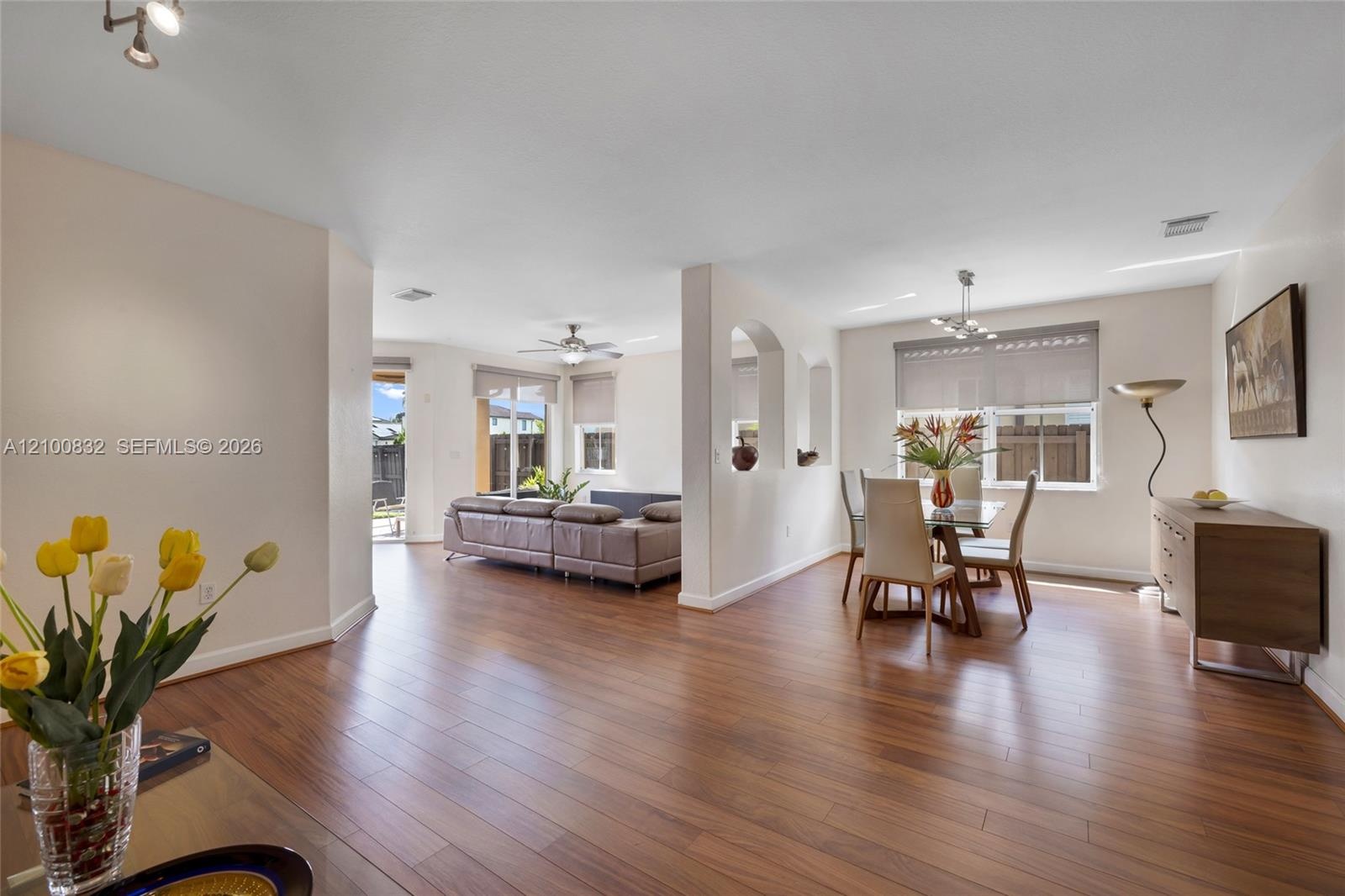 Open-concept interior featuring wood-finish flooring, architectural arched wall cutouts, recessed lighting, and multiple windows with installed roller