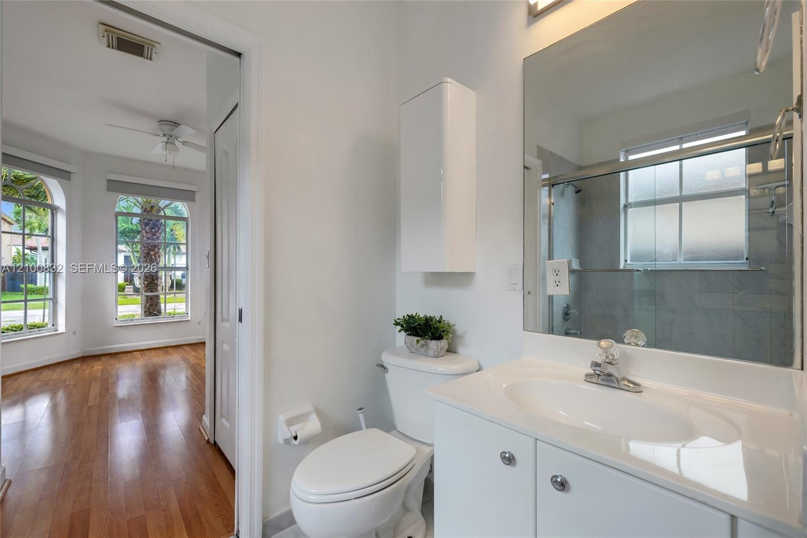 Bathroom featuring a white vanity with an integrated sink, a large wall-mounted mirror, a tub-shower combination with sliding glass doors, and a built
