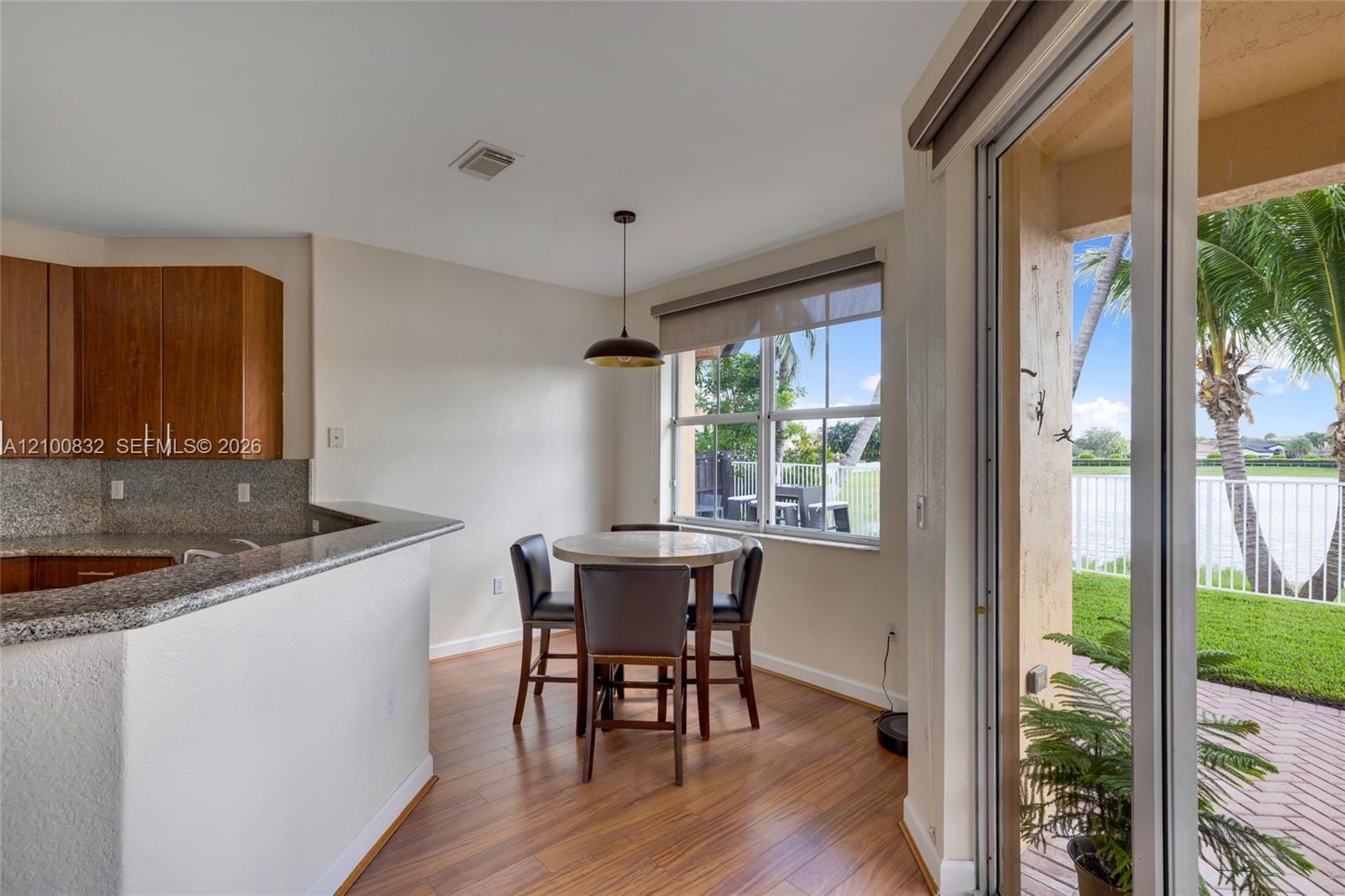 Kitchen featuring wood cabinetry, stone countertops, wood-finish flooring, a pendant light fixture, and sliding glass doors to a paved patio