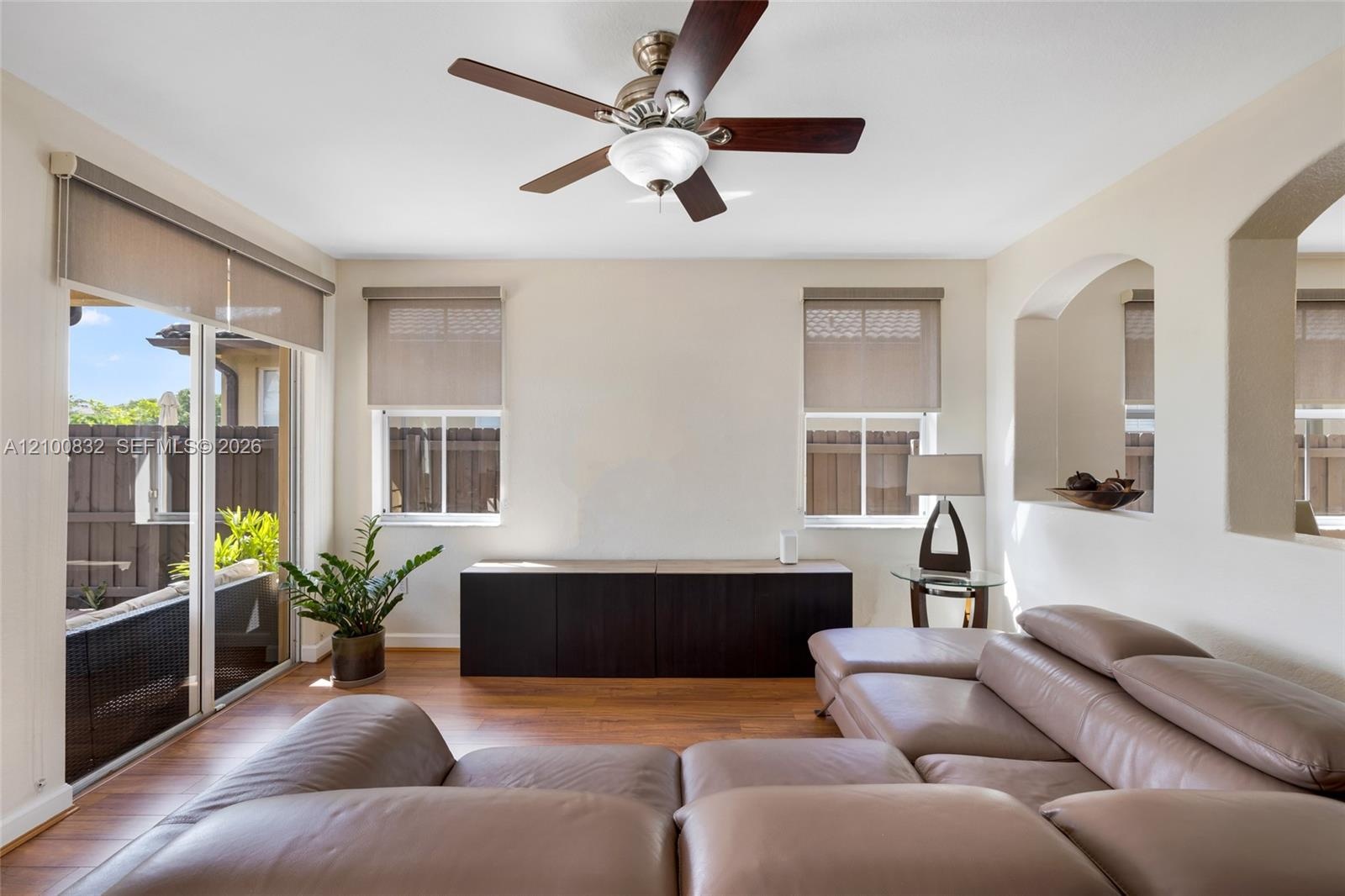 Living area featuring wood-finish flooring, recessed wall niches, and a multi-blade ceiling fan with integrated lighting
