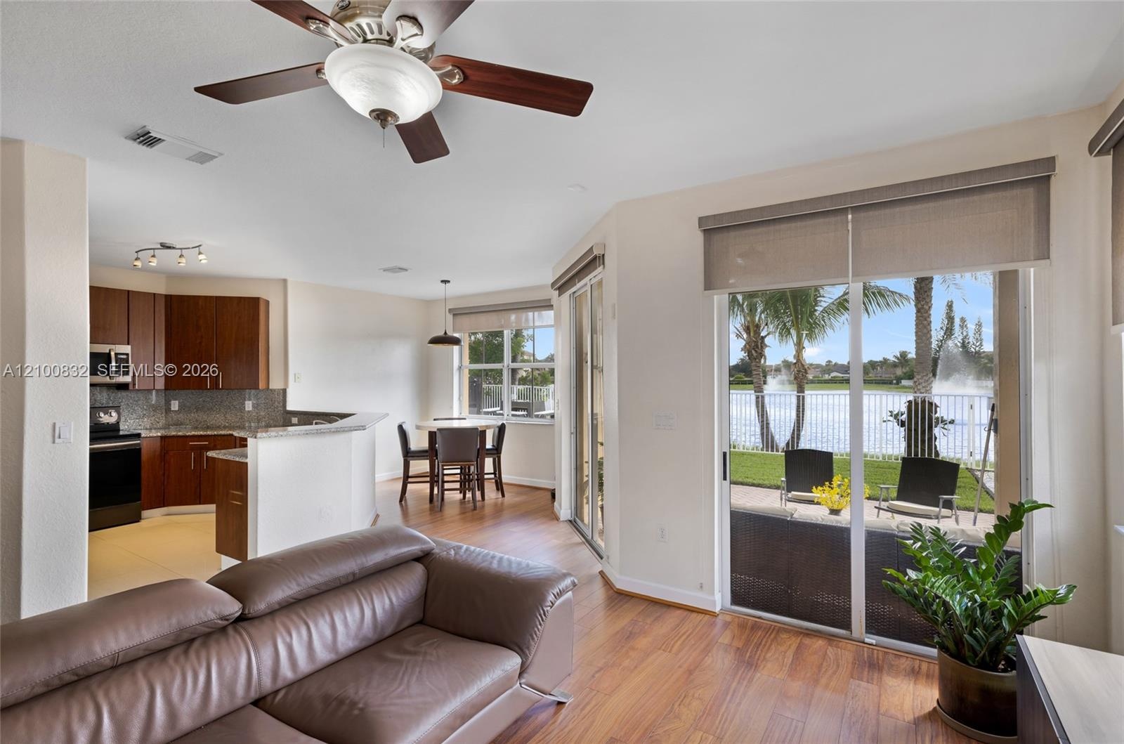 Open-concept interior featuring wood-finish flooring, cherry-toned cabinetry, stone-surface countertops, a ceiling fan with integrated lighting, and s