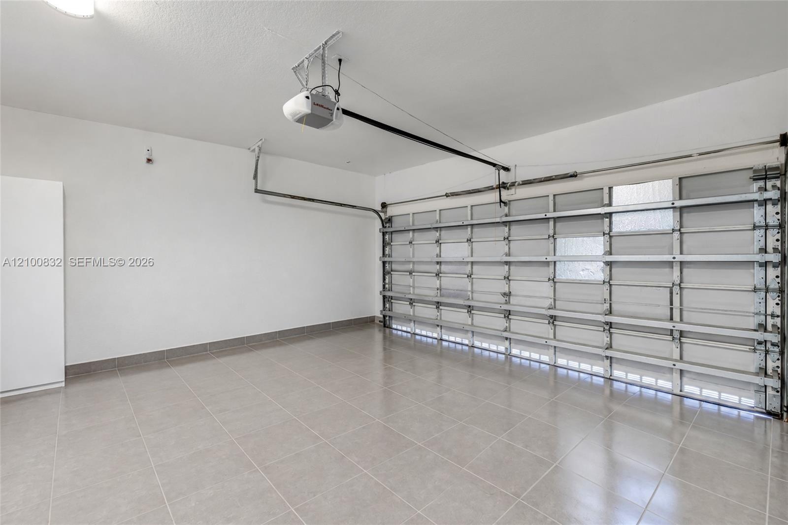Garage featuring finished tile flooring, white-painted walls, and an automated garage door opener system