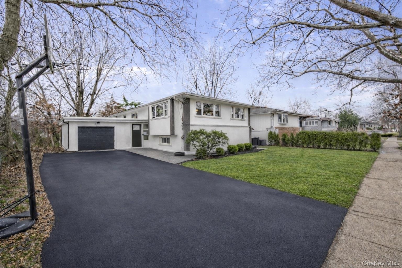 Split-level exterior featuring a light-toned facade, an attached garage with a dark-finished door, and an expansive asphalt driveway