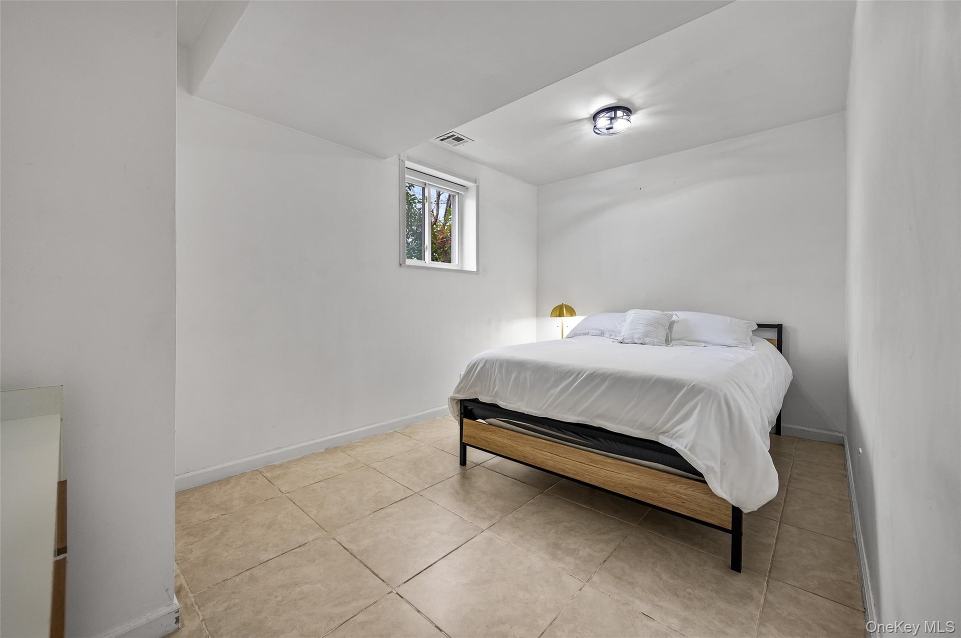 Neutral interior space featuring large-format ceramic tile flooring, a window with exterior exposure, and a flush-mount circular ceiling light fixture