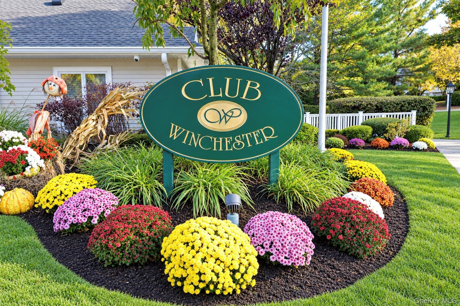 Community signage featuring oval club identifier, manicured landscaping, and mulch garden beds