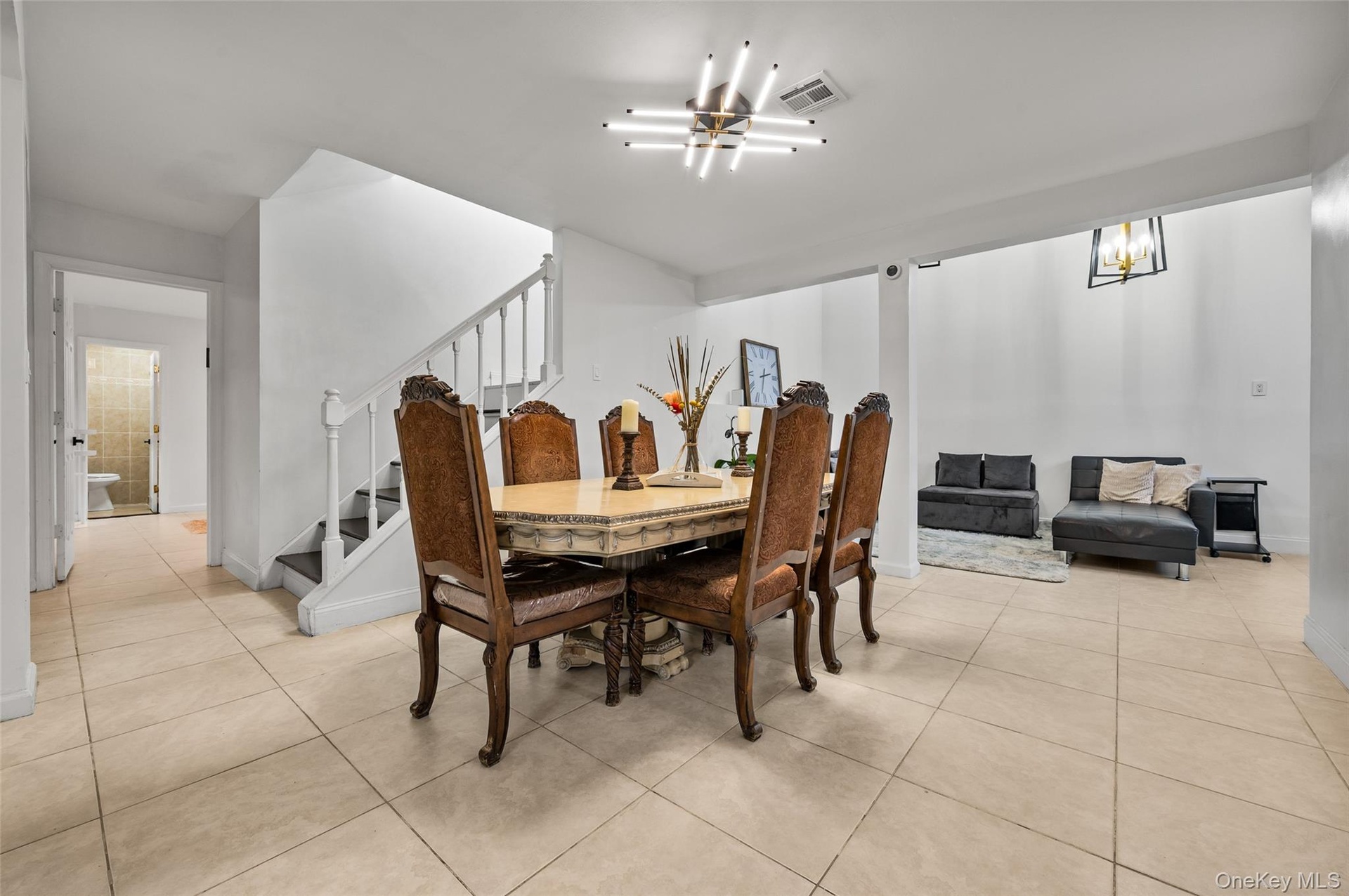 Large-format ceramic tile flooring, modern multi-arm linear ceiling fixture, and open staircase with white balusters