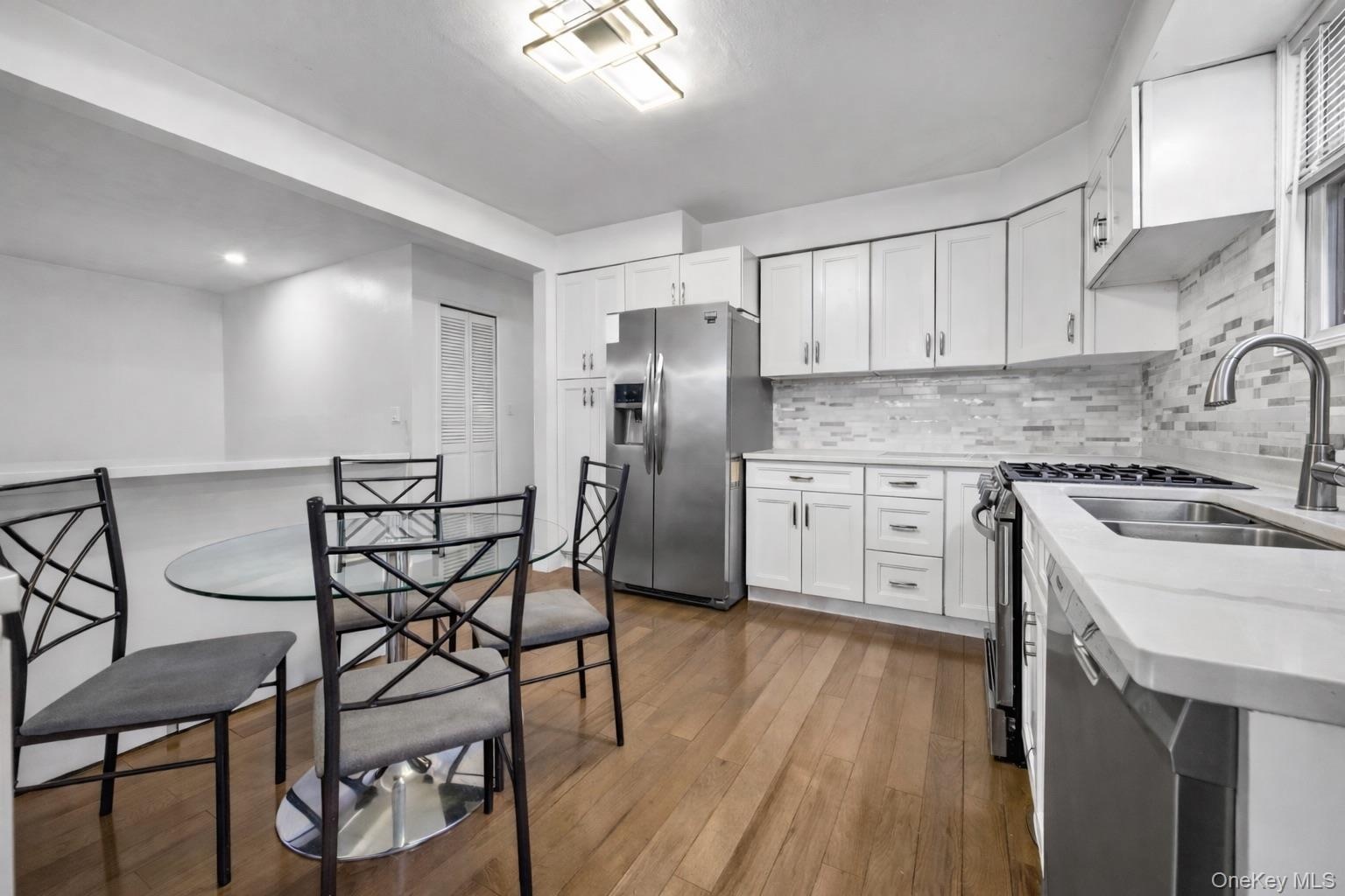 Kitchen featuring white cabinetry, wood-finish flooring, stone-style countertops, stainless steel appliances, and a glass tile backsplash