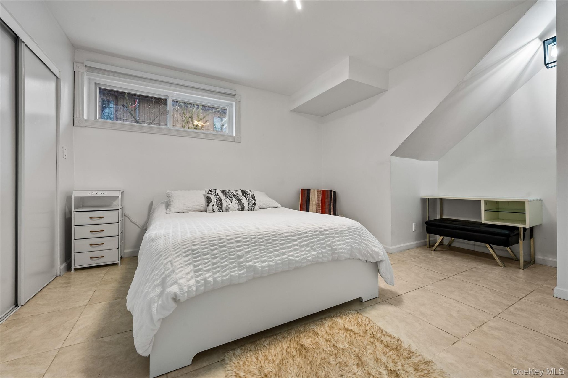 Neutral-toned tile flooring, sliding closet doors, and angled ceiling architecture