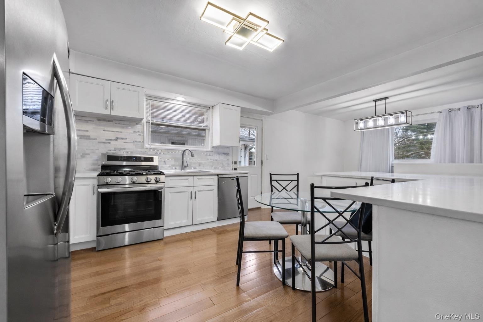 Kitchen featuring white cabinetry, wood-finish flooring, stainless steel appliances, tiled backsplash, and geometric overhead lighting