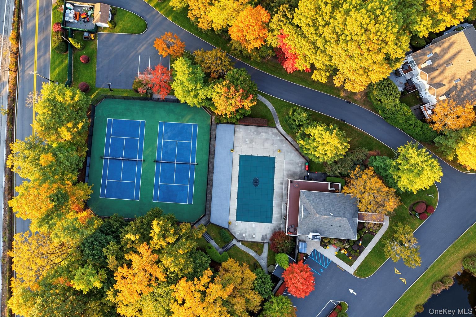 Aerial perspective of dual tennis courts and a swimming pool with a hardscape deck, surrounded by mature deciduous trees