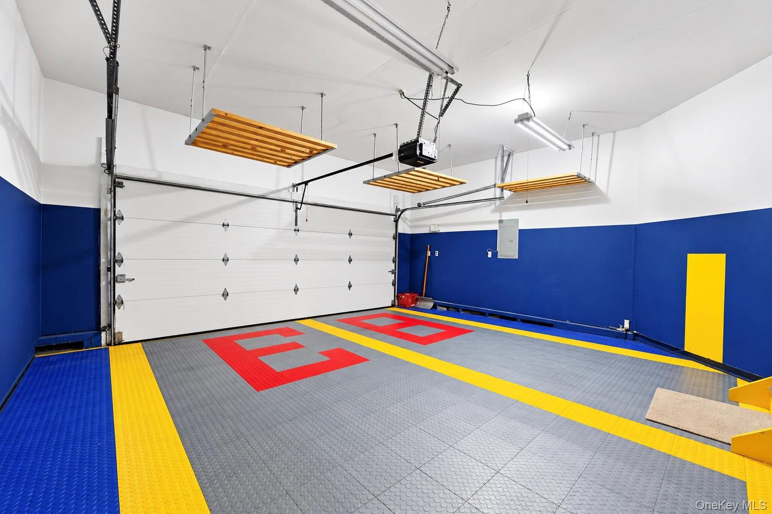 Garage interior featuring interlocking modular floor tiles, three overhead suspended storage platforms, automated roll-up door, and high-contrast pain