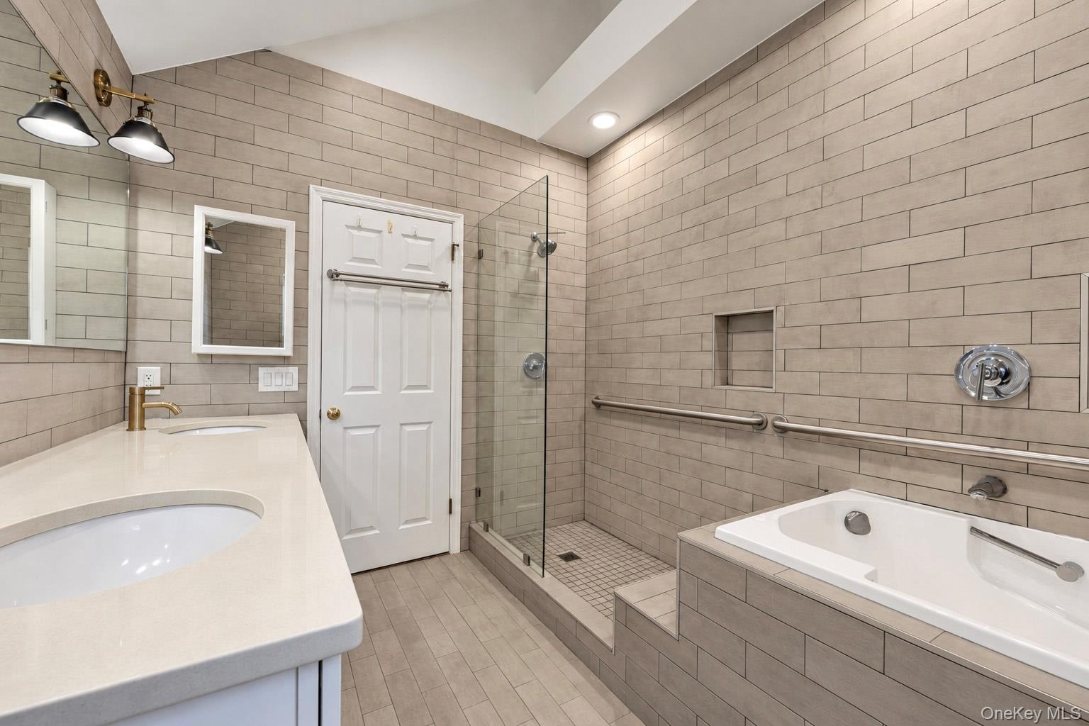 Bathroom featuring horizontal tile wall cladding, a walk-in shower with a glass enclosure, a built-in soaking tub, quartz countertop vanity, and vault