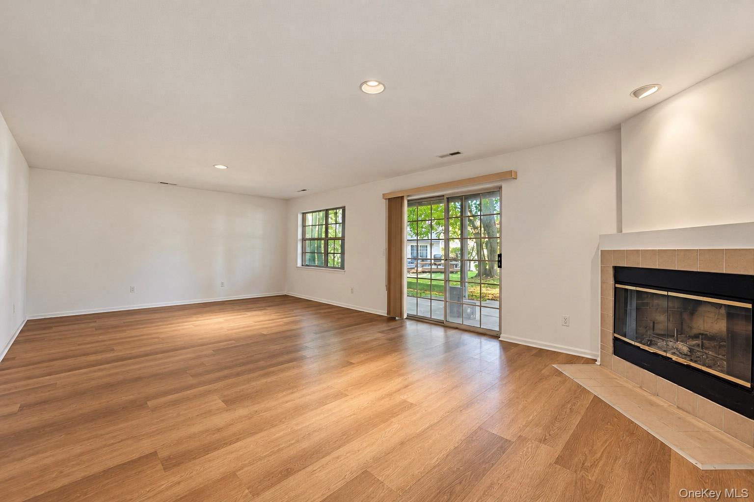 Spacious living area featuring wood-finish flooring, recessed lighting, a tile-surround fireplace, and sliding glass doors
