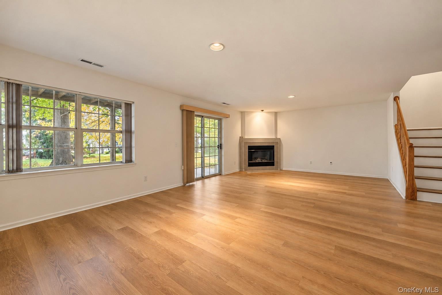 Open-concept interior featuring wood-finish flooring, a corner fireplace with a stone-surround mantel, recessed lighting, expansive multi-pane windows